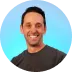 Smiling man with short dark hair wearing a dark shirt against a blue gradient background.